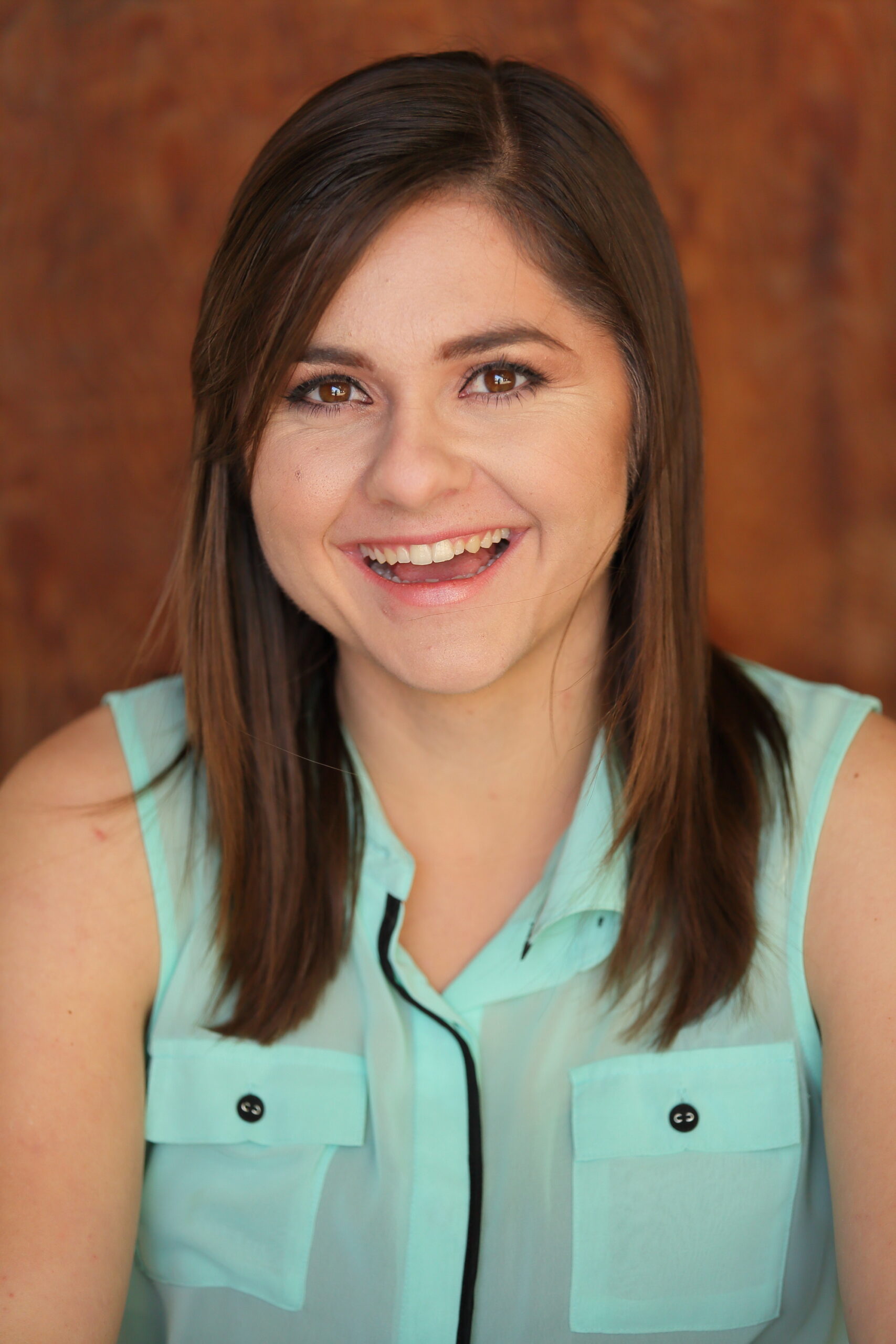 Melissa Marino smiling on a brown background with a mint green, sleeveless collar shirt